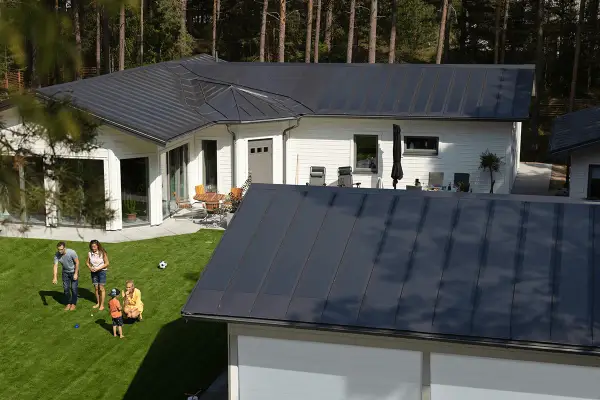Familj njuter av solen på gräsmattan framför ett modernt hus med ett stilrent lindab solar roof.