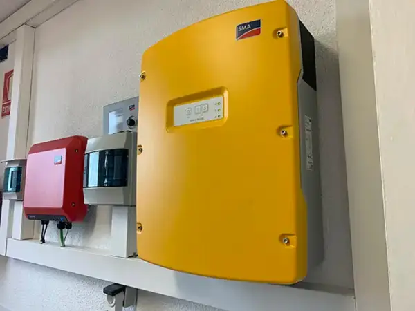 Gul SMA solcellsväxelriktare, en röd enhet och en grå enhet monterade på en vägg. En solig dag för att maximera din sunny tripower.
